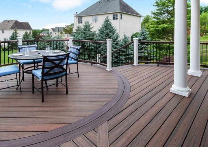 Curved composite deck with dining set and elegant railing, offering scenic suburban views.