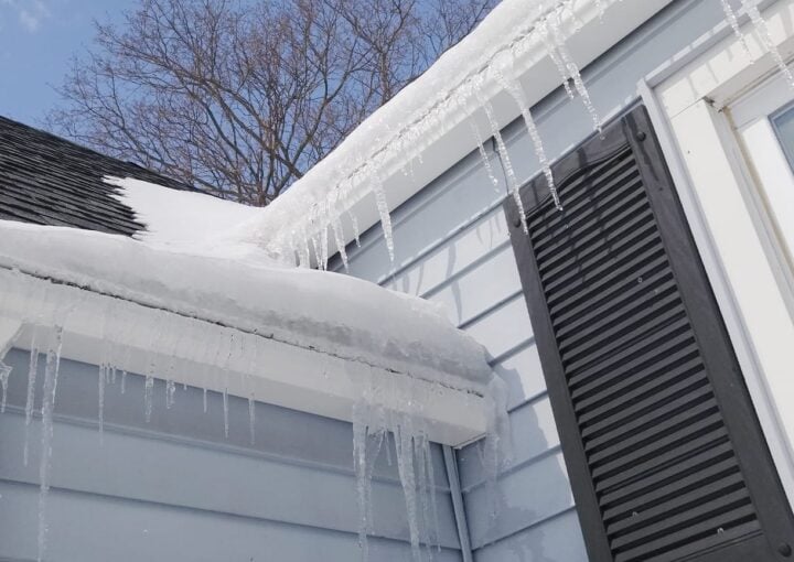 snow-covered roof with icicles showing winter damage risks to home gutter systems
