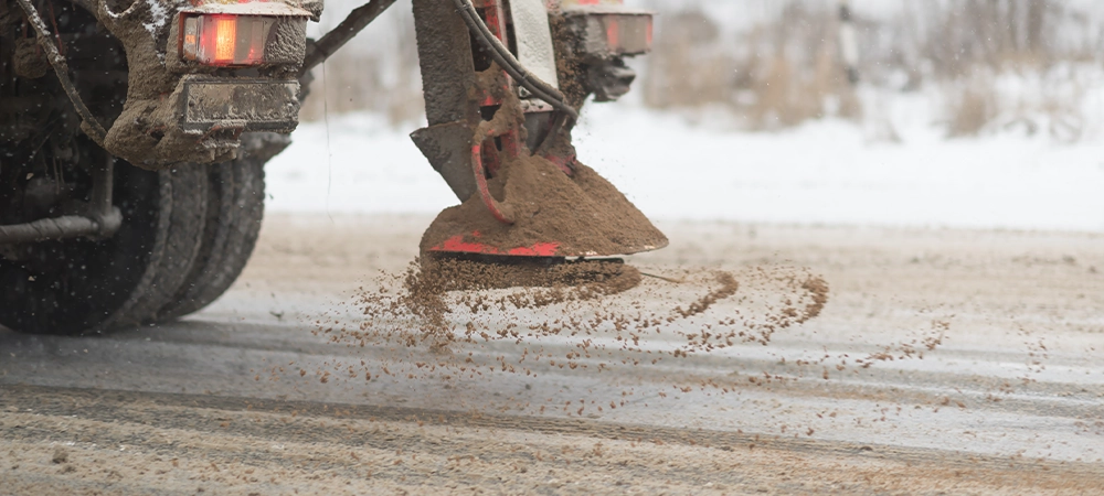 view from the car behind orange highway maintenance truck spreading de-icing salt and sand