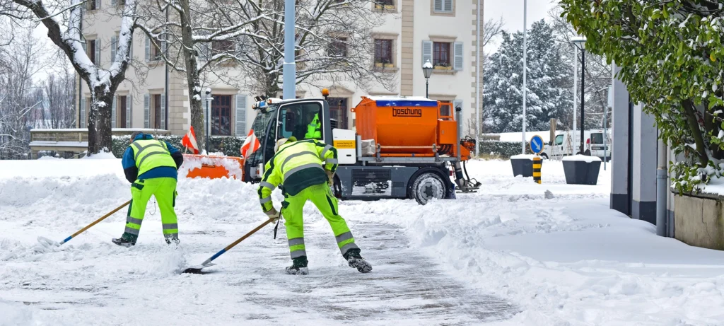 The two workers and one tractor removing the white fresh fluffy snow from the road,