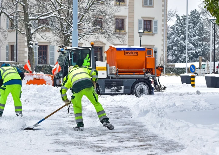 The two workers and one tractor removing the white fresh fluffy snow from the road,