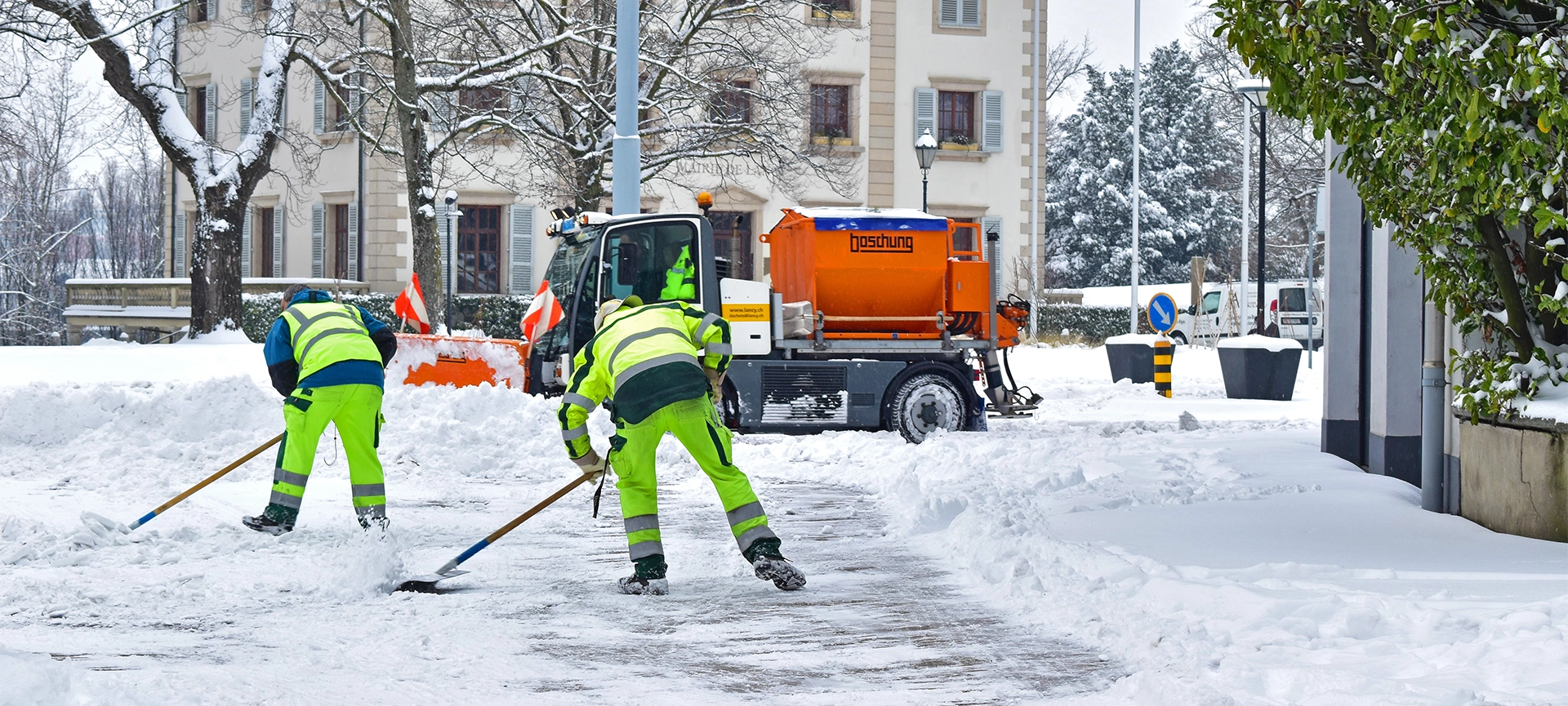 The two workers and one tractor removing the white fresh fluffy snow from the road,