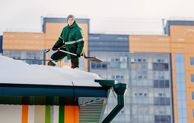 professional snow removal man on roof top of building