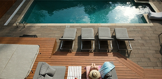 concrete pool image two women sitting on chair in wooden deck look at pool. concrete pool with interlocking surface