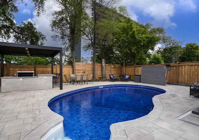 pool with interlock surface in backyard, open kitchen, water drainage system, wooden fence covered full yard with landscaping