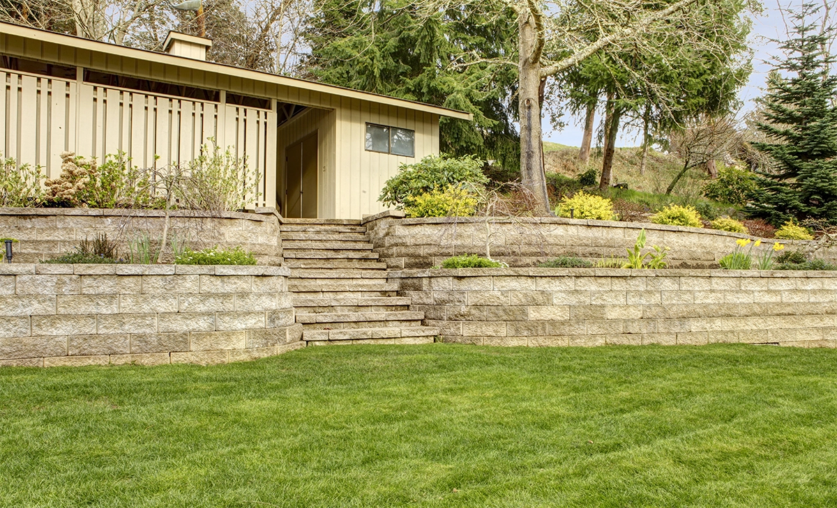multi level interlocking retaining walls with steps and building view in back lawn, prevention of trees and planting soil erosion