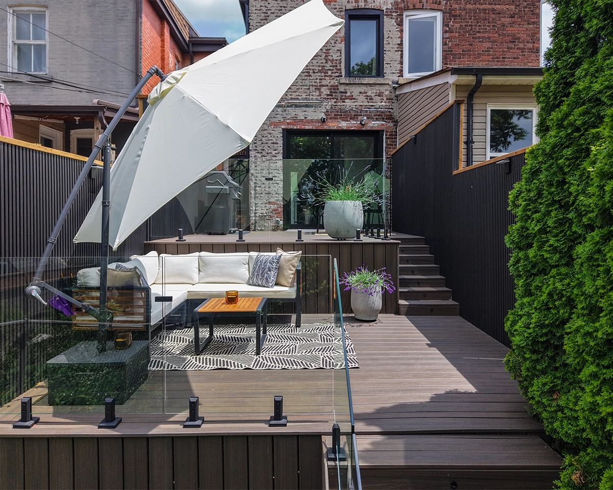 backyard front view, multi level deck with glass railing and modern fence. sitting setup and bbq system