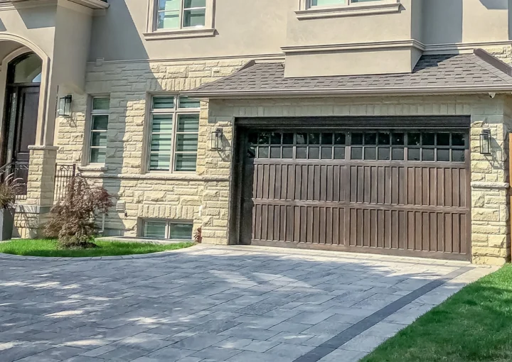 A beautiful large modern custom executive residential house with grey stone and brick, with gray shingles and grey trim, patterned interlock walkway and driveway, and double garage doors.