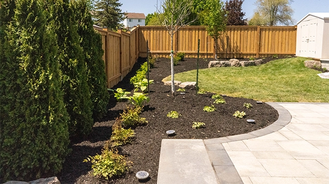 mulch for plants and tree with sodding, interlock patio and wooden fence in home backyard. landscaping, soft scaping
