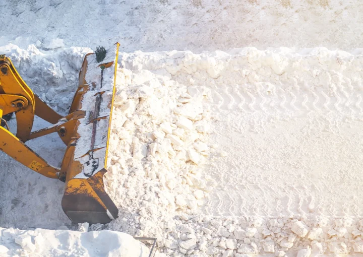 A large orange tractor removes snow from the road and clears the sidewalk. Cleaning and clearing roads in the city from snow in winter. Snow removal after snowfalls and blizzards.
