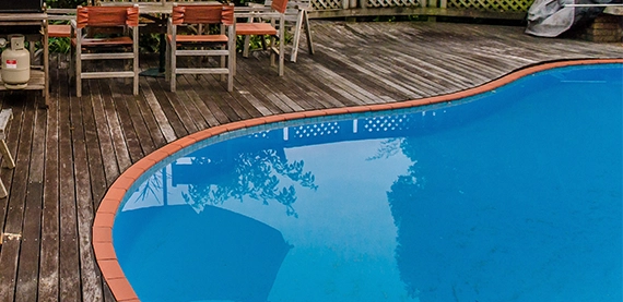 vinyl pool with orange coping with old wooden deck