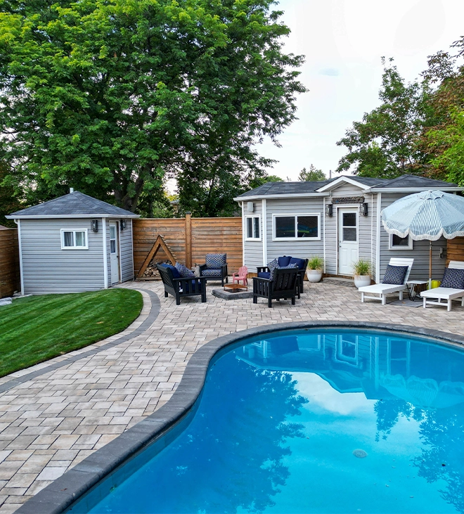 well designed pool deck interlocking surface around swimming pool, custom carpentry, wooden fence and sitting setup in backyard