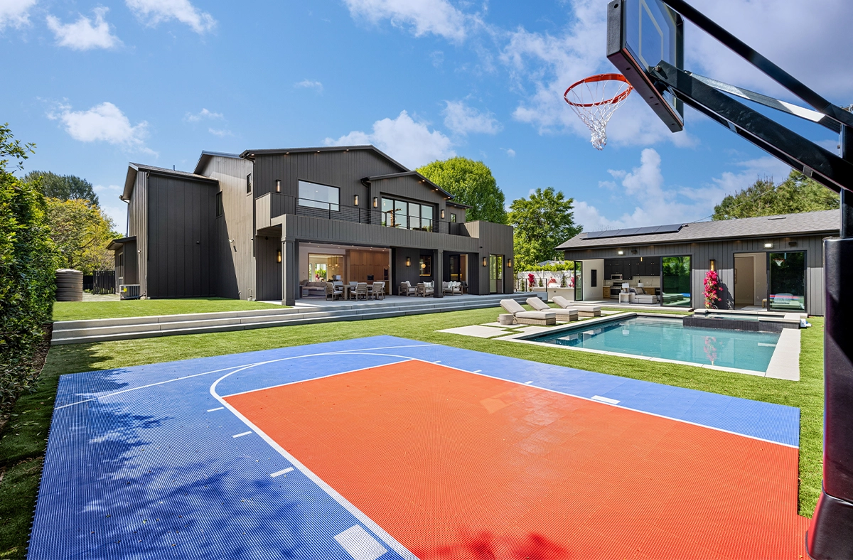 sport court convenience Modern luxury house with a basketball court and swimming pool in the backyard under a clear blue sky.
