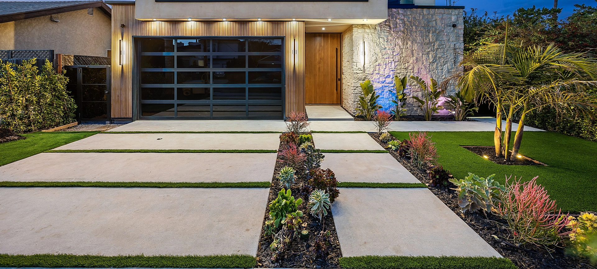 Modern two-story house with a well-lit exterior and landscaped front yard featuring palm trees and succulents.