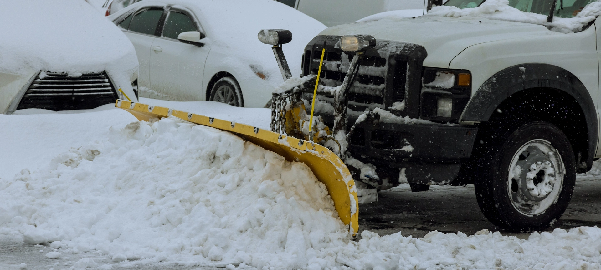 During heavy snowfall, snowplow truck removes snow from parking lot