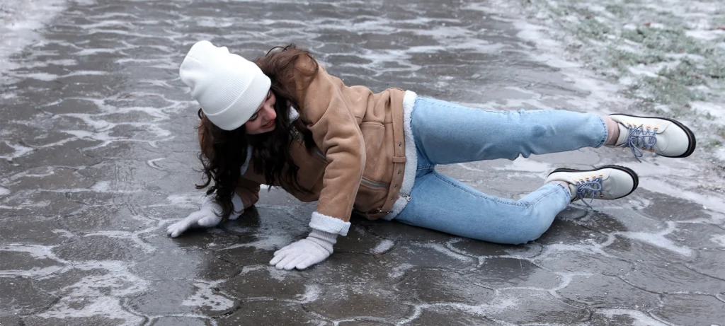 Young woman fallen on slippery icy pavement outdoors