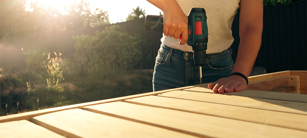 Female carpenter at work using hand drilling machine. Female carpenter building a wooden cabinet with an electric drill