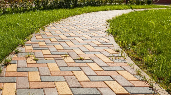 The pedestrian path is paved with multi-colored paving stones. Grass grows between the tiles. Selective focusing.