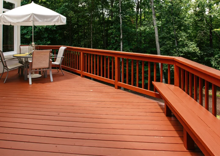 Large Wooden Deck Featuring an Umbrella-Covered Outdoor Dining Set Surrounded by A Dense Forest in Summer