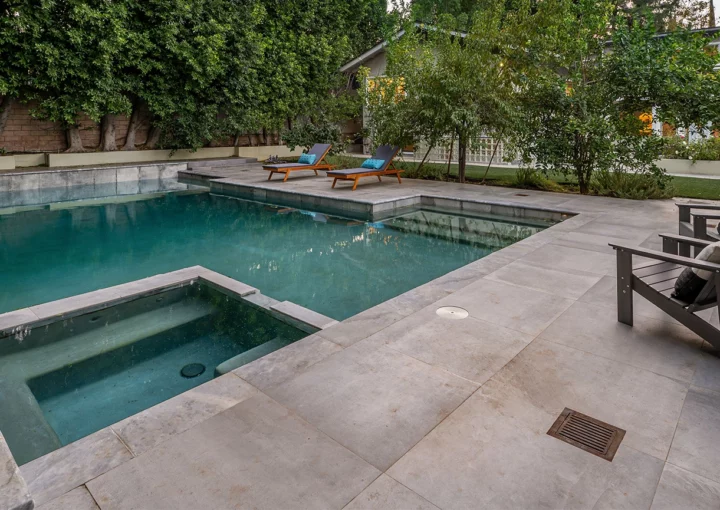 Modern backyard with a swimming pool, lounge chairs, and lush green trees