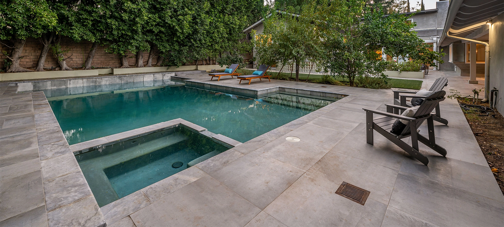 Modern backyard with a swimming pool, lounge chairs, and lush green trees