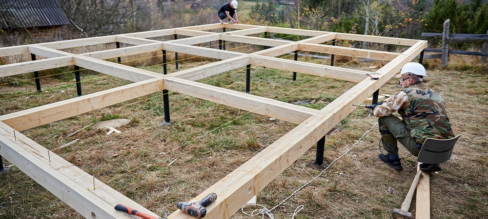 Man worker building wooden frame house on pile foundation.