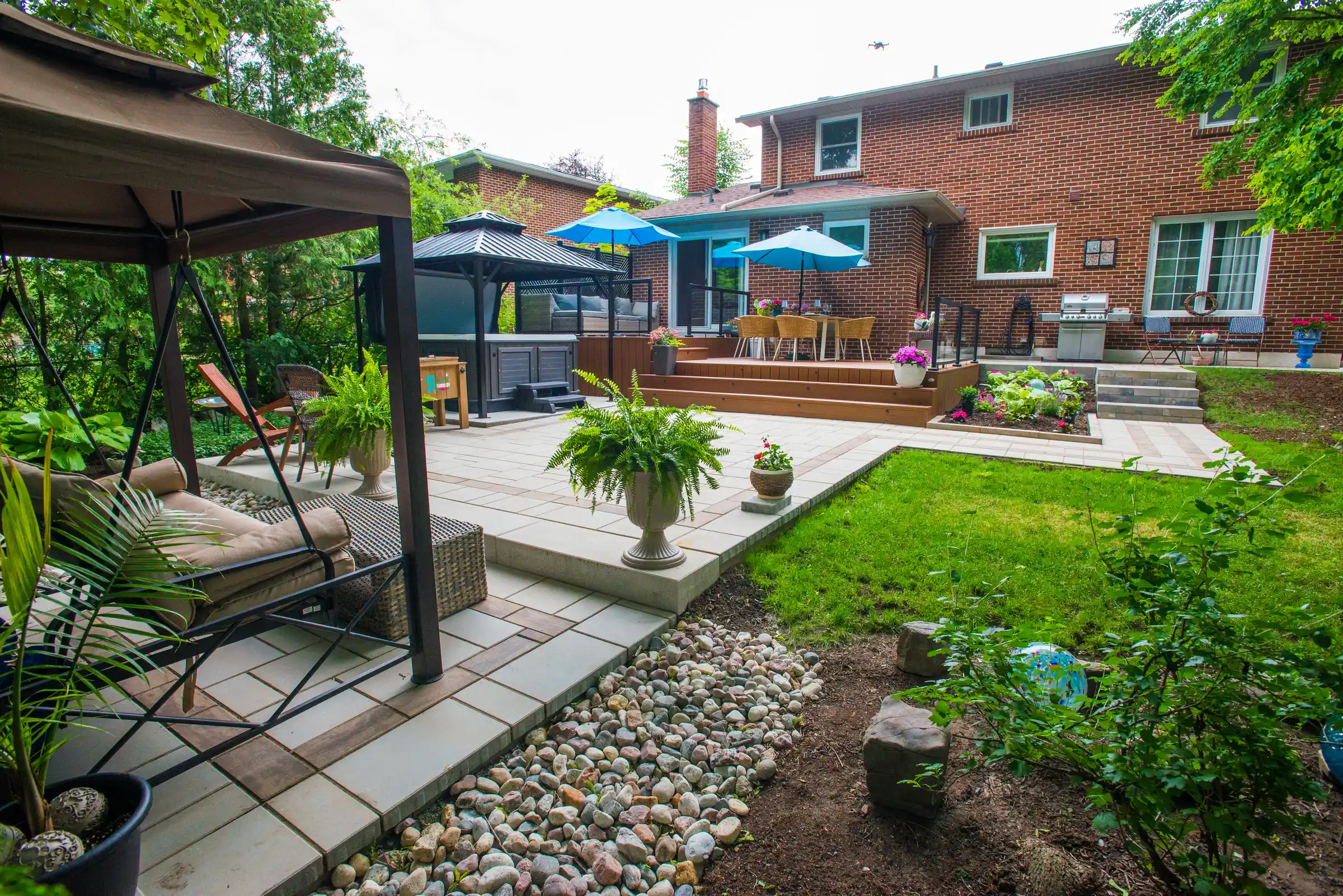 composite deck with glass railing and some flower pots along with a gazebo with a hot tub