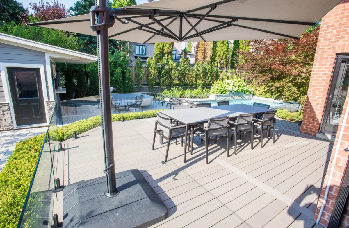 deck-dining-umbrella-pool-glass-railing Composite deck dining area with glass railing beside a pool