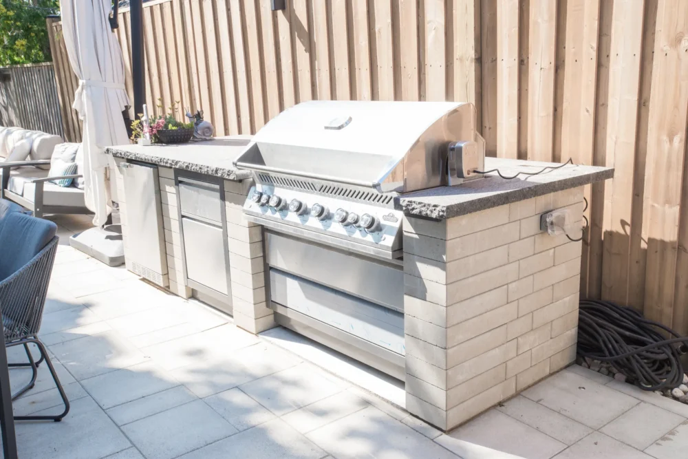 Outdoor kitchen with built-in grill and fridge on interlocking patio