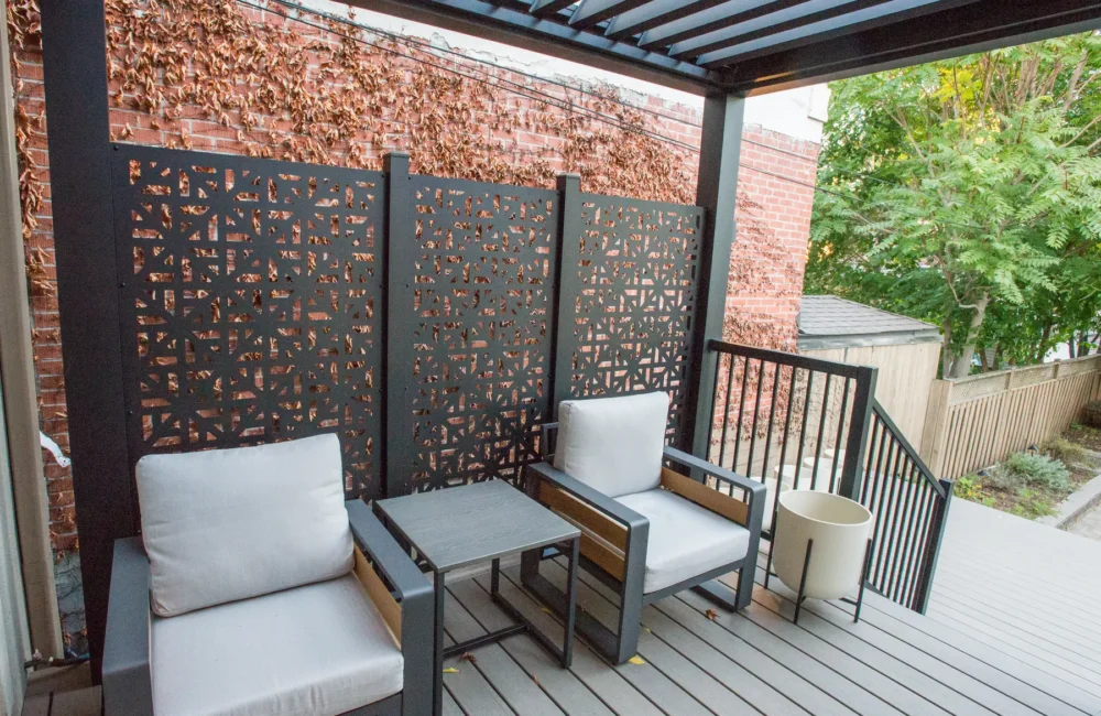 Lounge chairs under the electric pergola beside a decorative privacy screen