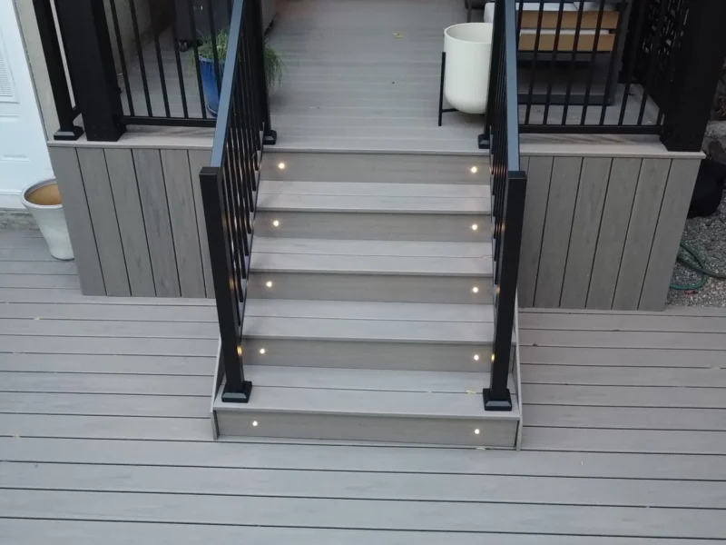 Lit Trex deck steps with black railing to the rear door